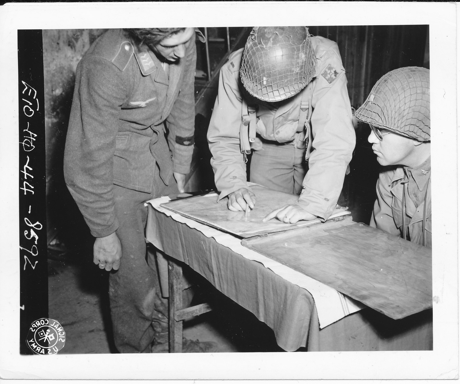 Lt. Walter V. Bodlander (hidden behind the helmet) taken on July 25, 1944 at St. Lo, France, interrogating a German POW and interpreting for Lt. Col. Hansen, G-2 for the 4th Infantry Division